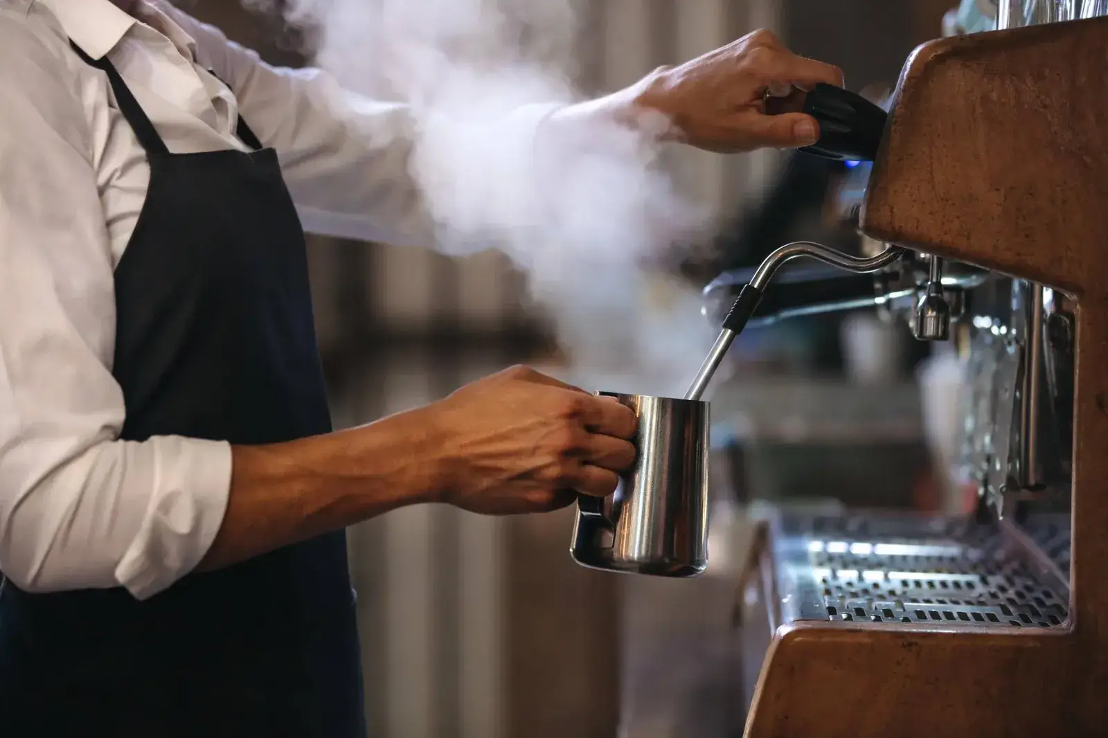 A barista steaming milk in a stainless steel jug at an espresso machine