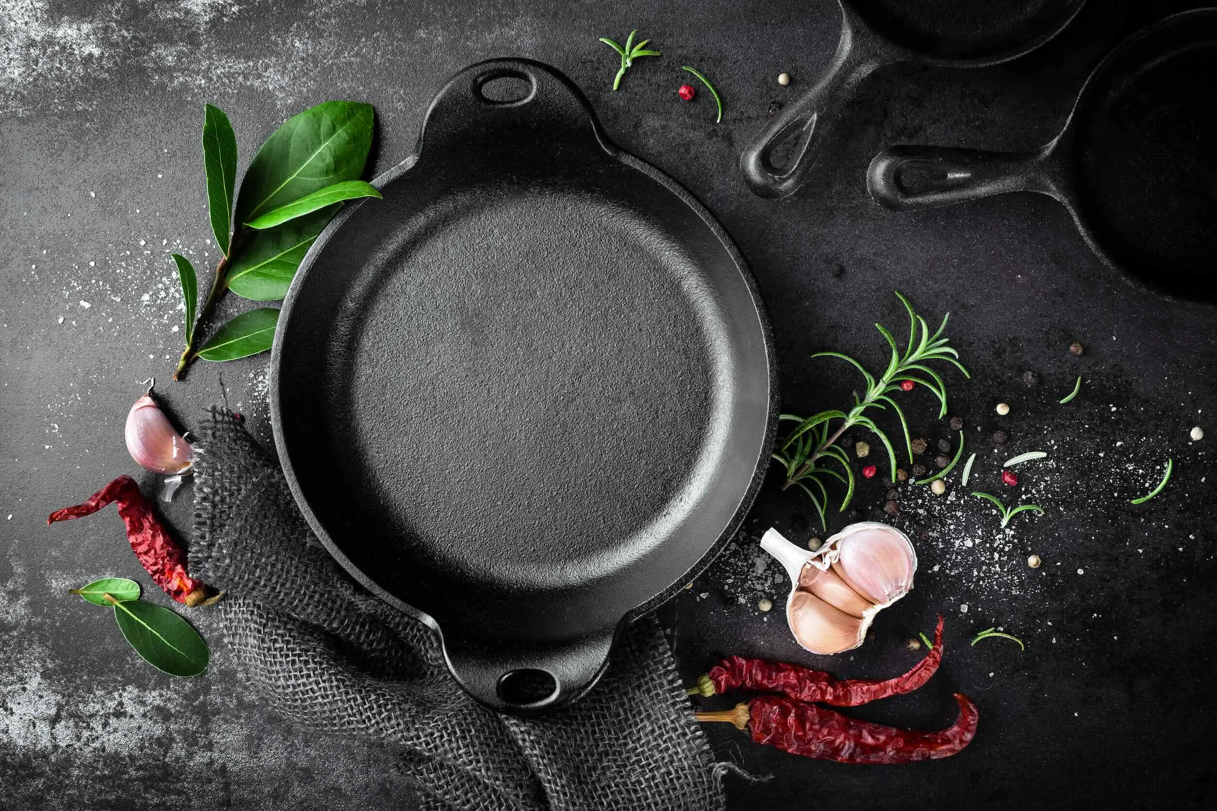 A cast iron skillet on dark slate with fresh herbs and garlic
